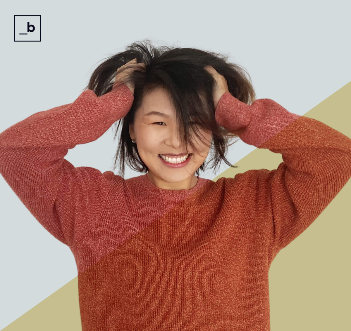 Woman in red sweater looking forward smiling, with her hands in her hair.